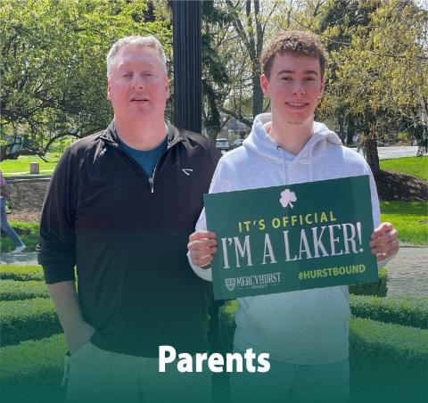 A dad posing with his son who has decided to attend ˽ֲ. The son holds a poster reading "It's Official. I'm a Laker!"